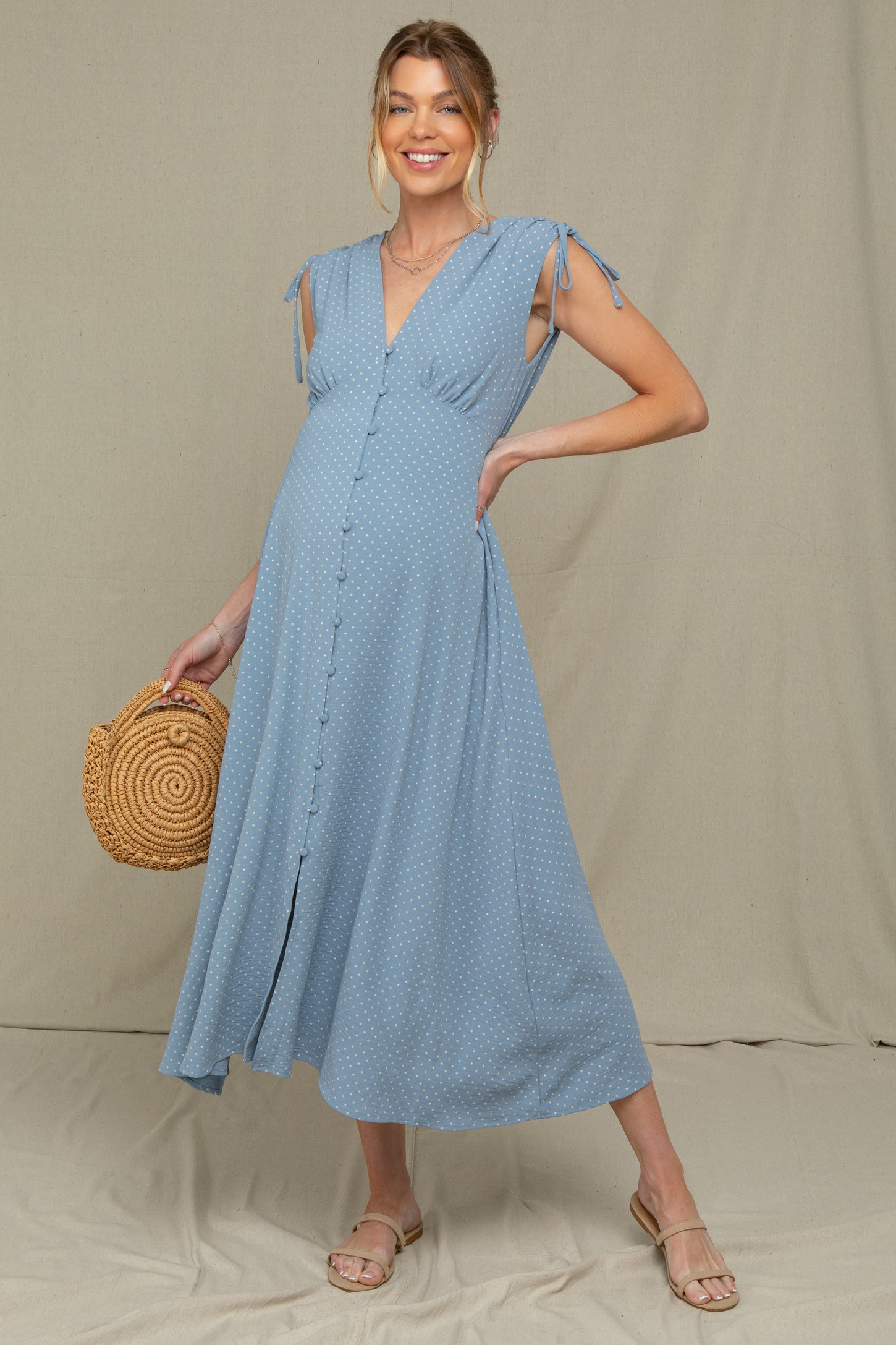 woman wearing a light blue polka dot maternity dress with tie sleeves and a baby bump, holding a woven bag