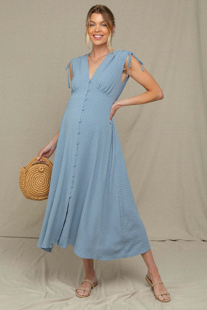 woman wearing a light blue polka dot maternity dress with tie sleeves and a baby bump, holding a woven bag