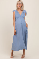 woman wearing a light blue maternity dress with tie straps, button details, and pockets, showcasing her baby bump