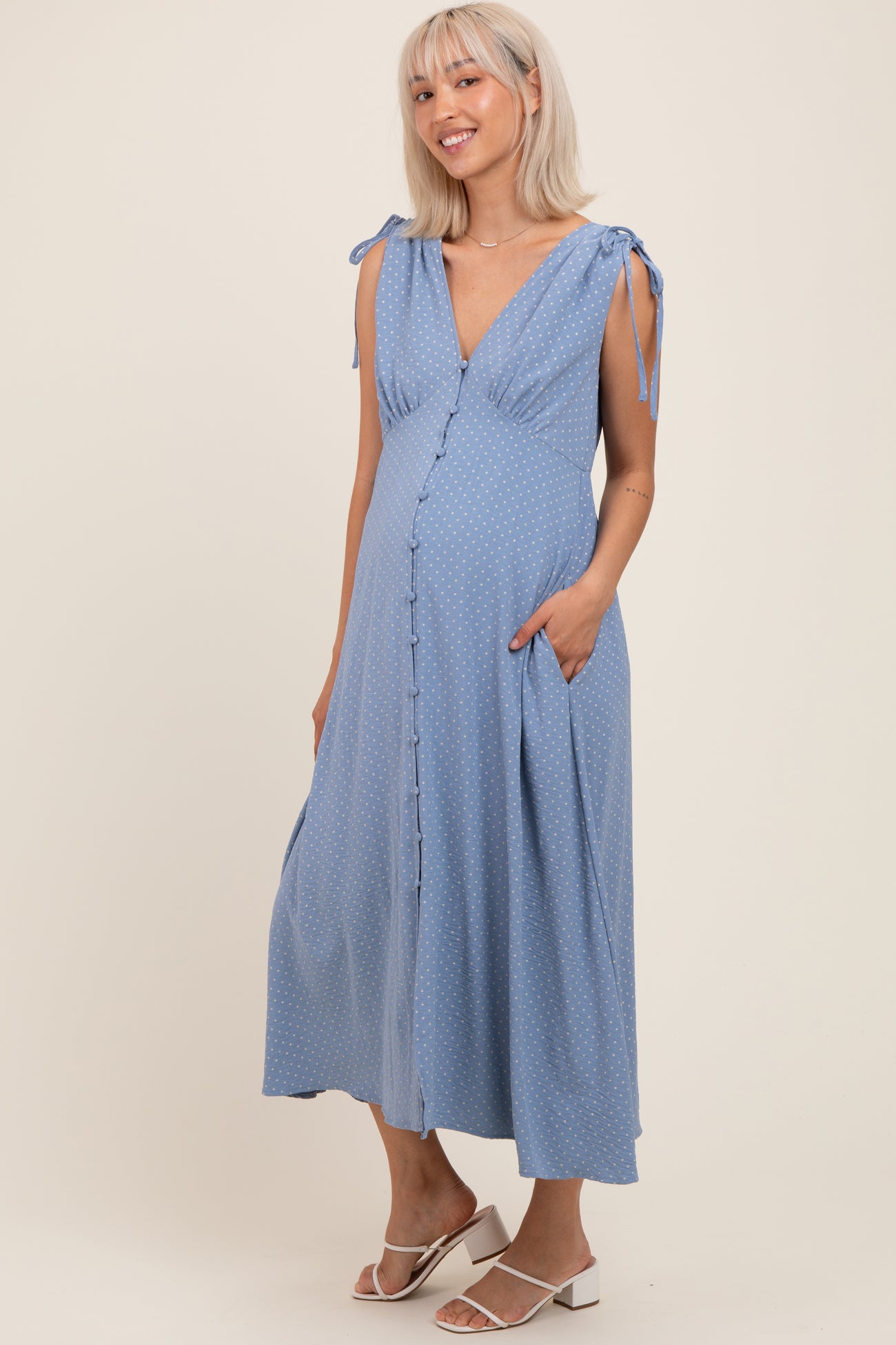 woman wearing a light blue polka dot maternity dress with tie straps and side pockets, showcasing her baby bump