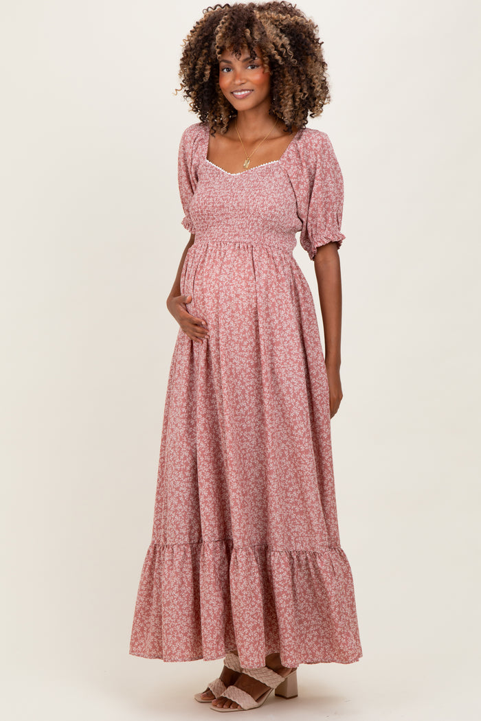 woman wearing a pink floral maternity maxi dress with puff sleeves and a flowing skirt, holding her baby bump