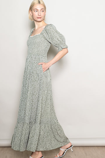 woman wearing a light green floral maxi dress with puff sleeves and side pockets, standing sideways against a neutral background