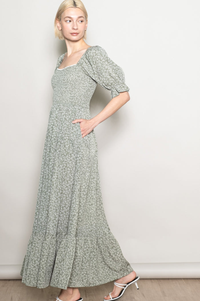 woman wearing a light green floral maxi dress with puff sleeves and side pockets, standing sideways against a neutral background