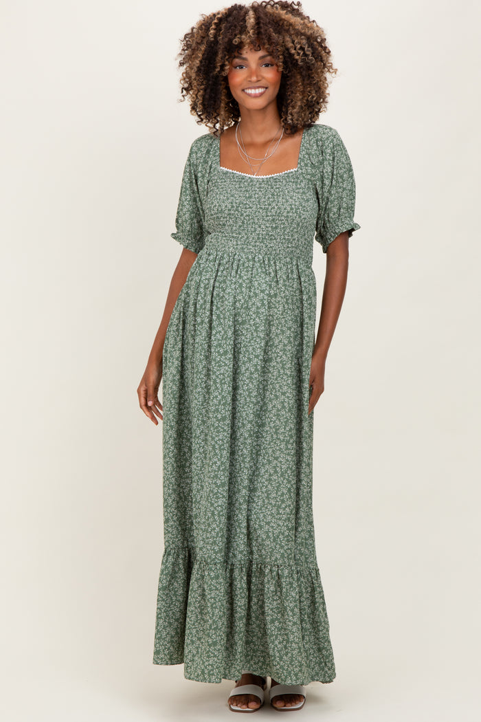woman wearing a green floral maternity dress with puff sleeves and a ruffled hem, smiling at the camera