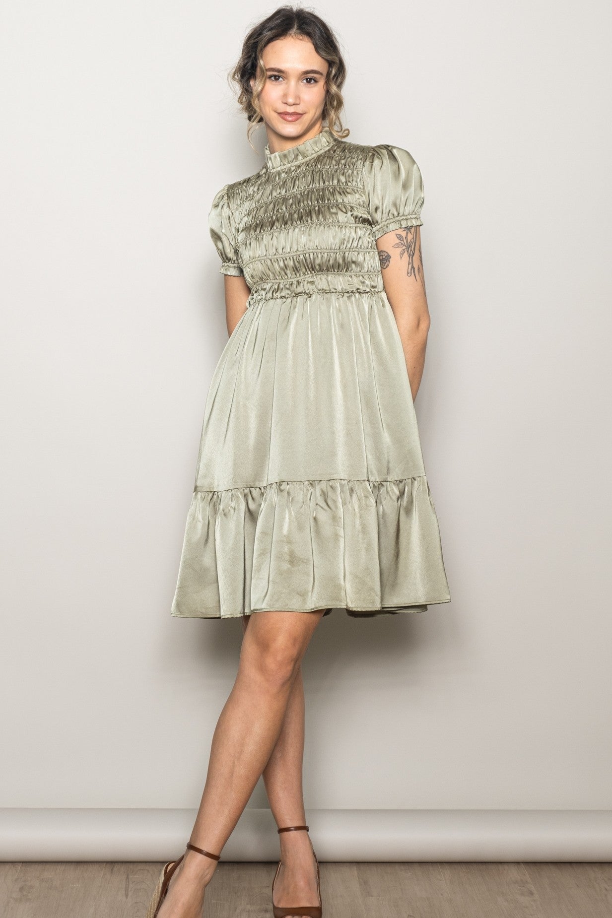 woman wearing a sage green short sleeve smocked dress with a tiered skirt and a high neckline