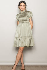 woman wearing a sage green short sleeve smocked dress with a tiered skirt and a high neckline
