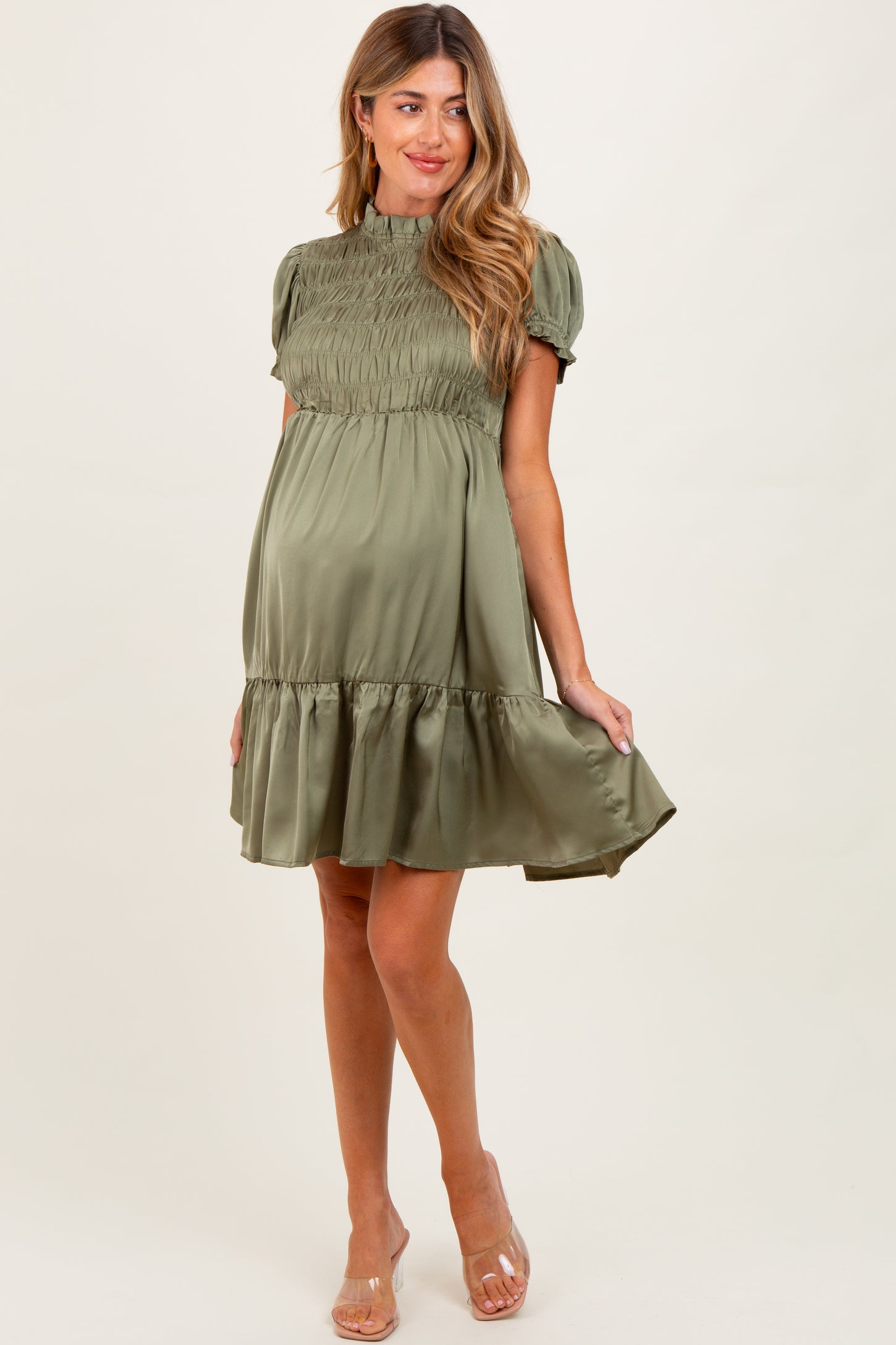 woman wearing a sage green short sleeve maternity dress with a smocked bodice and flared skirt, showing her baby bump