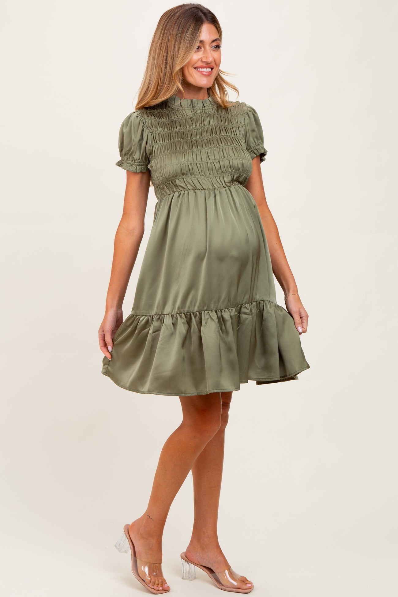 woman wearing an olive green short sleeve smocked maternity dress with a ruffled hem and visible baby bump