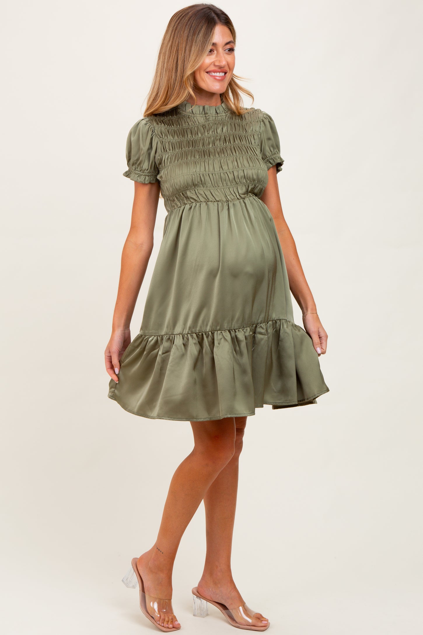 woman wearing an olive green short sleeve smocked maternity dress with a ruffled hem and visible baby bump