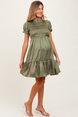 woman wearing an olive green short sleeve smocked maternity dress with a ruffled hem and visible baby bump