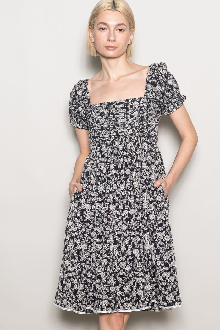 woman wearing a black floral puff sleeve dress with a square neckline and pockets