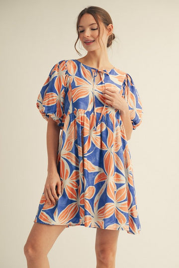 woman wearing a blue and orange floral print puff sleeve mini dress with a tie detail at the neckline
