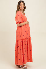 woman wearing a coral floral embroidered maternity maxi dress and holding her baby bump