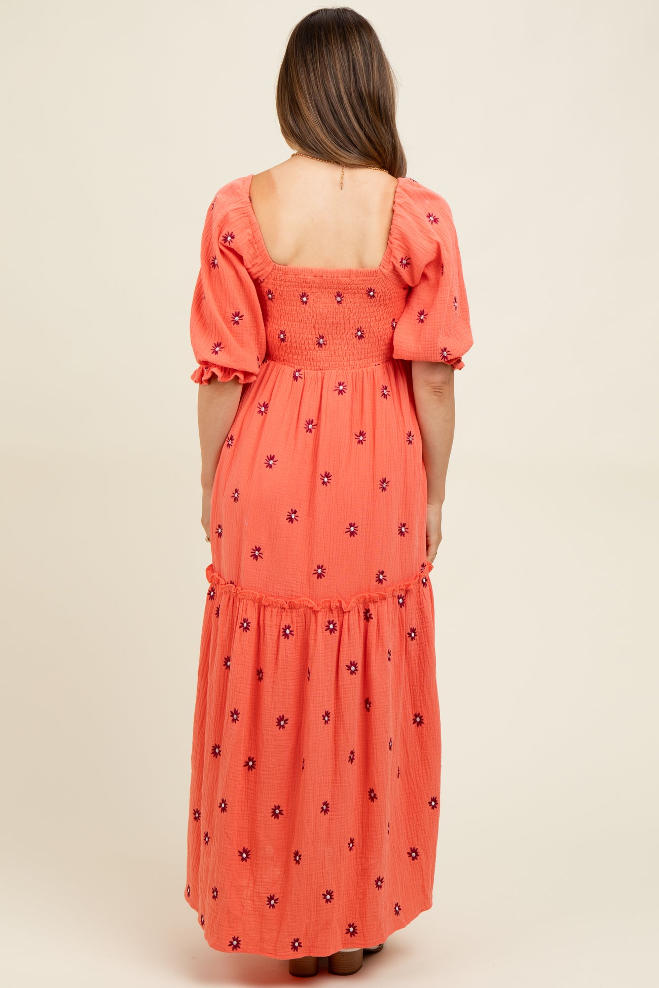 woman wearing a coral maternity maxi dress with puff sleeves and floral embroidery, showing the back view