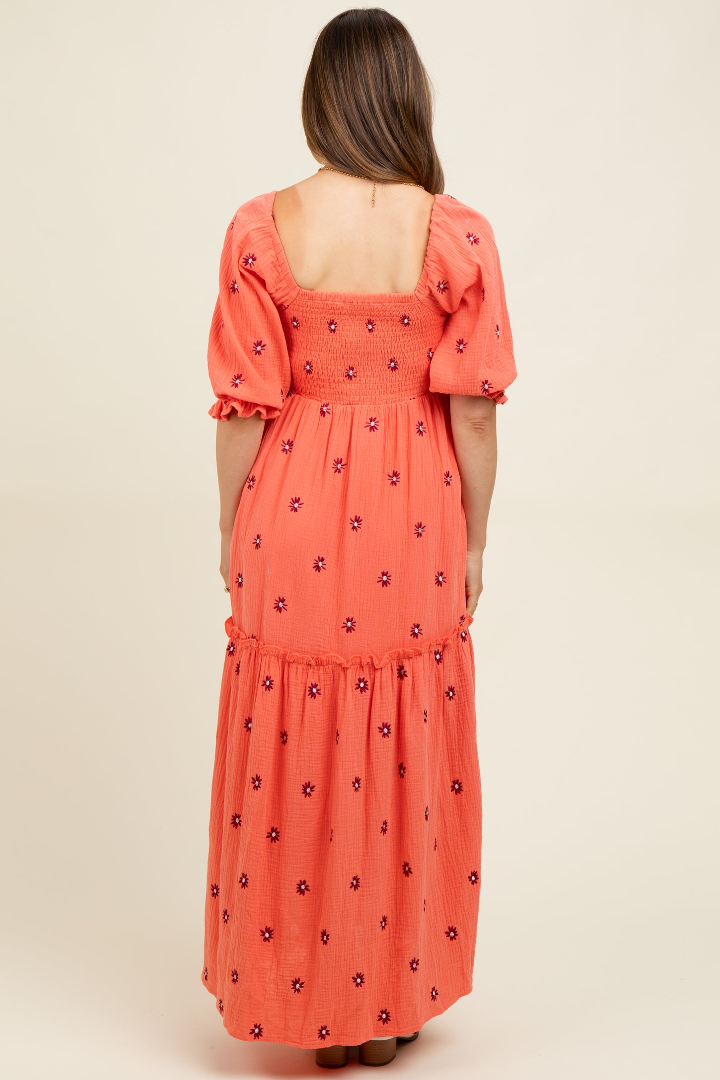woman wearing a coral maternity maxi dress with puff sleeves and floral embroidery, showing the back view