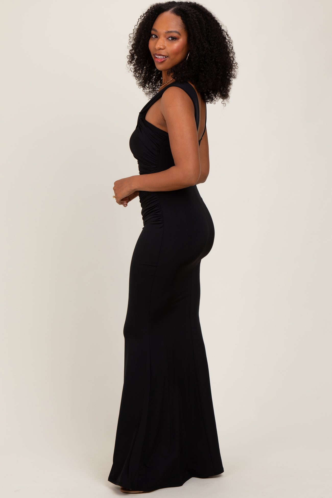 woman wearing a black sleeveless fitted dress with ruched sides and a flared skirt, posed from the side