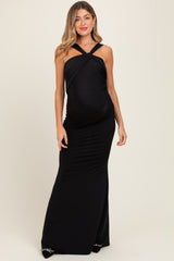woman wearing a black maxi maternity dress with a halter neck and ruching detail accentuating a baby bump