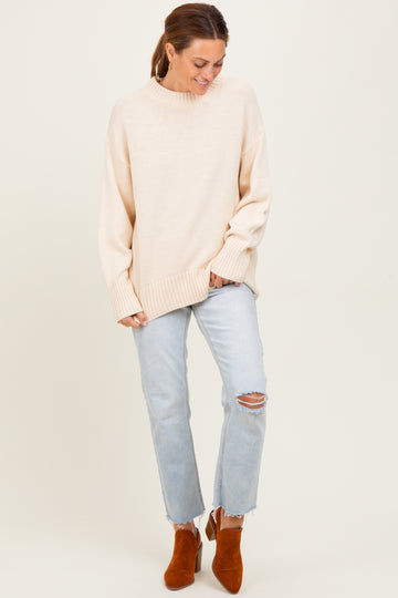 woman wearing a light beige oversized sweater with ribbed details and paired with light blue ripped jeans and brown ankle boots