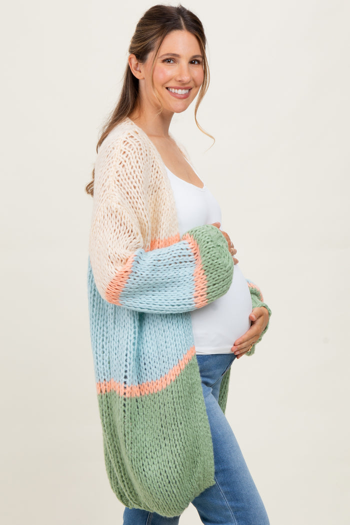woman wearing a multi-colored chunky knit maternity cardigan and showing her baby bump while smiling
