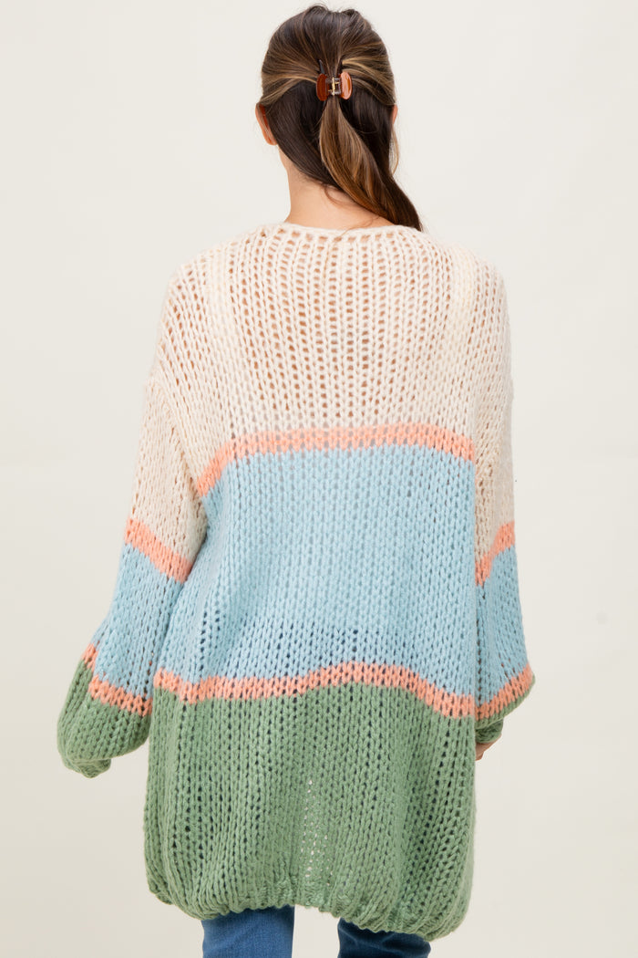 a woman in a multicolored oversized knit maternity sweater featuring pastel stripes in blue, pink, and green, with open weave.