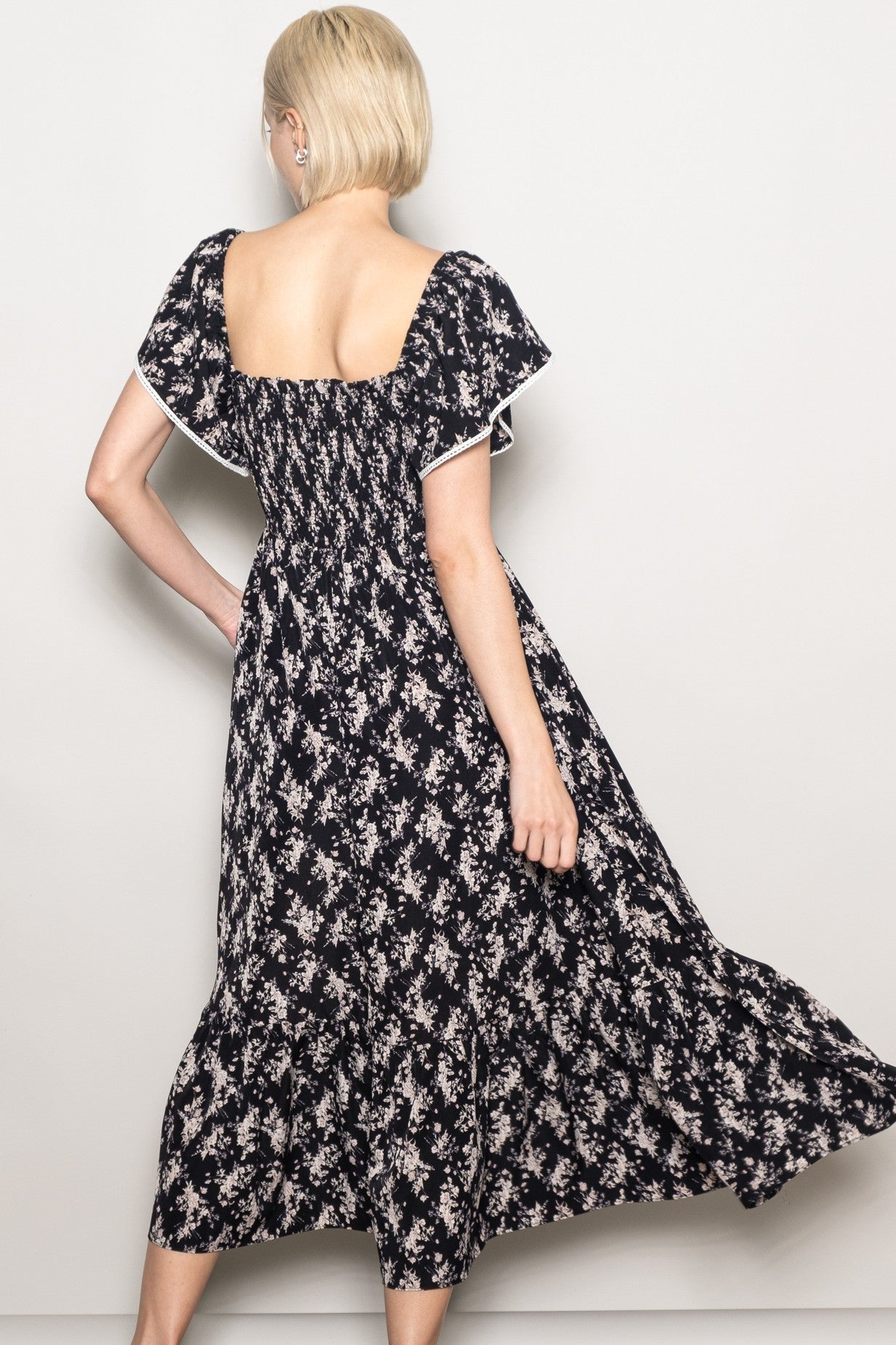 woman wearing a black floral maxi dress with a square neckline and flutter sleeves, seen from the back