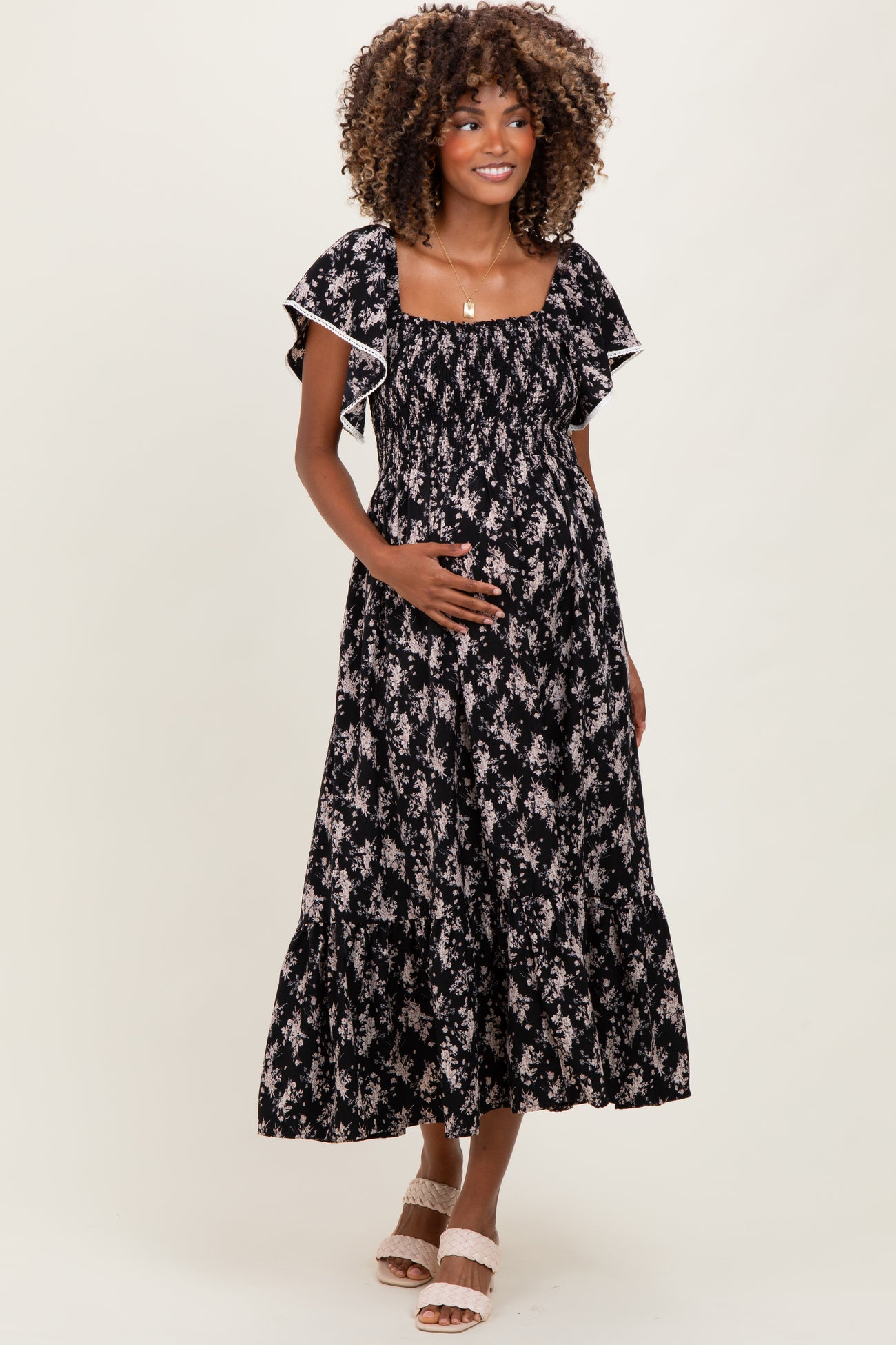 woman wearing a black floral print maternity maxi dress and holding her baby bump