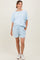 woman wearing a light blue maternity short set with a loose top and shorts, featuring pockets