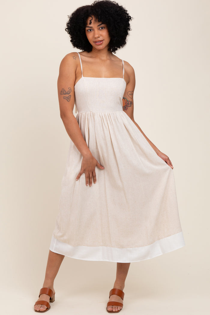 woman wearing a beige midi dress with spaghetti straps and a white hem, posing with one hand on her hip