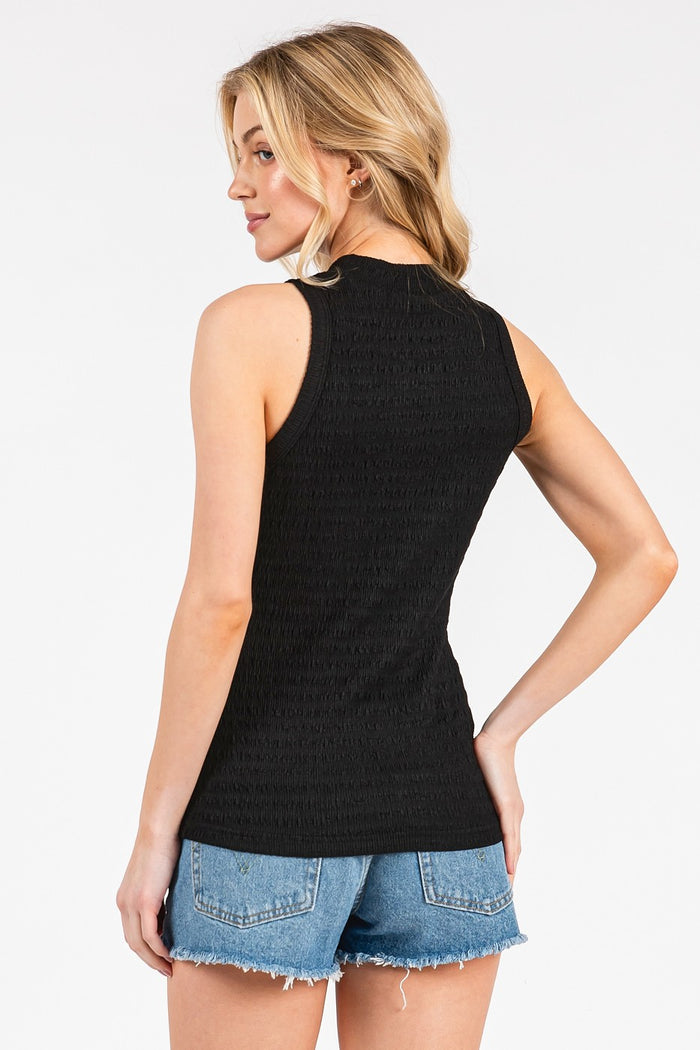 woman wearing a black sleeveless top with ruching at the back paired with denim shorts