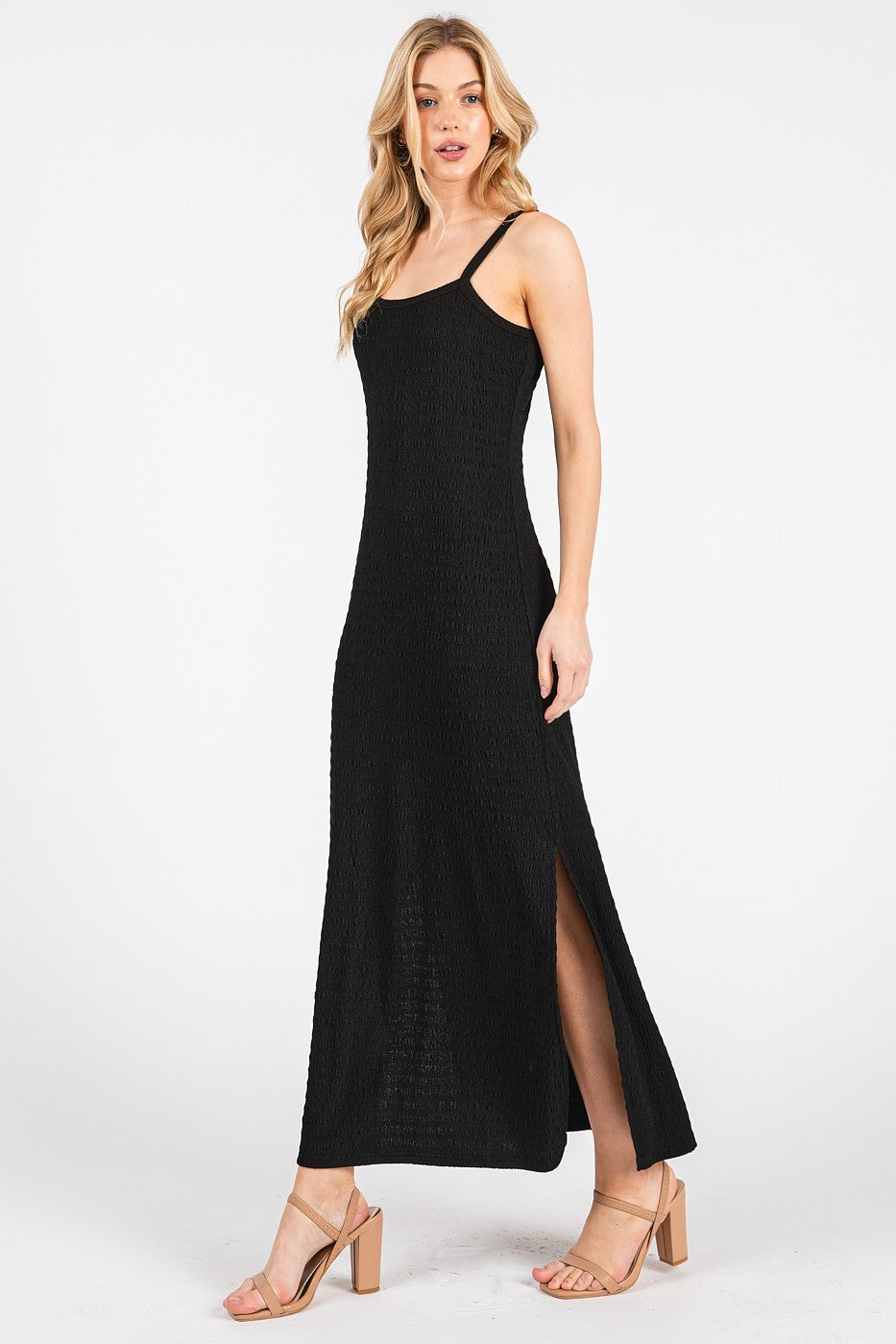 woman wearing a black maxi dress with a fitted bodice, thin straps, and side slits, paired with beige heels