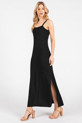 woman wearing a black maxi dress with a fitted bodice, thin straps, and side slits, paired with beige heels