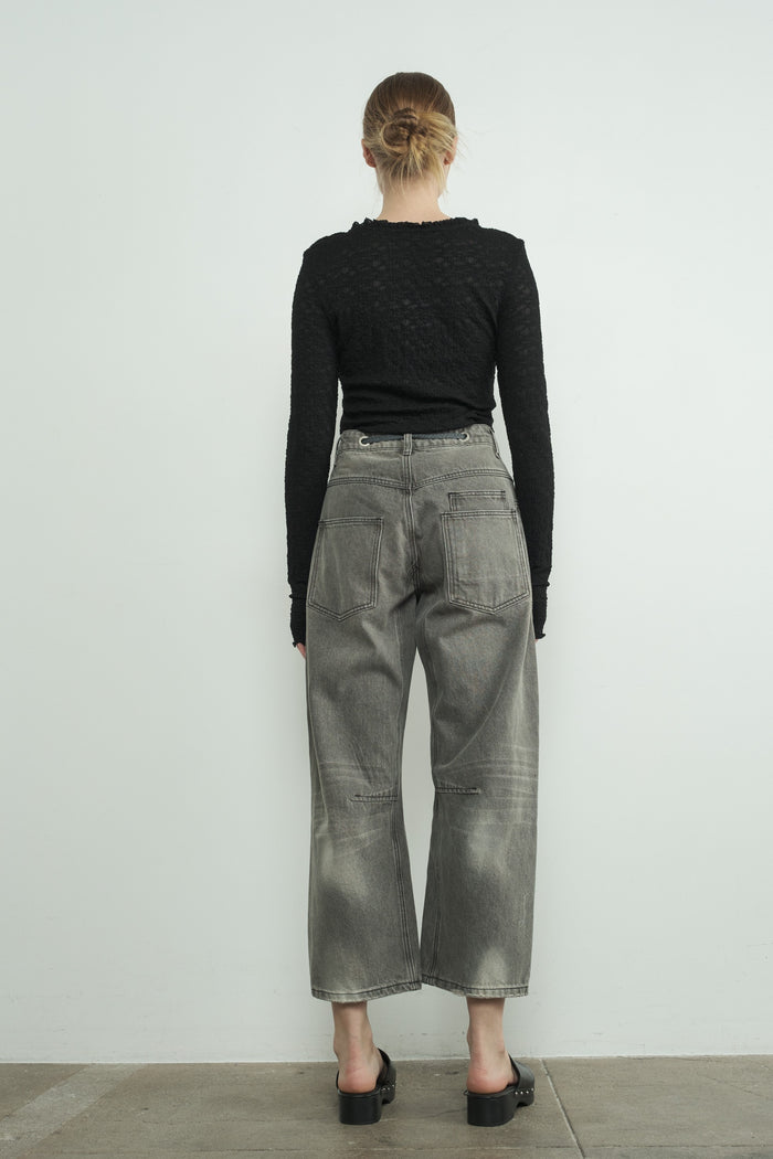 woman wearing a black textured long sleeve top and gray wide leg jeans, seen from the back