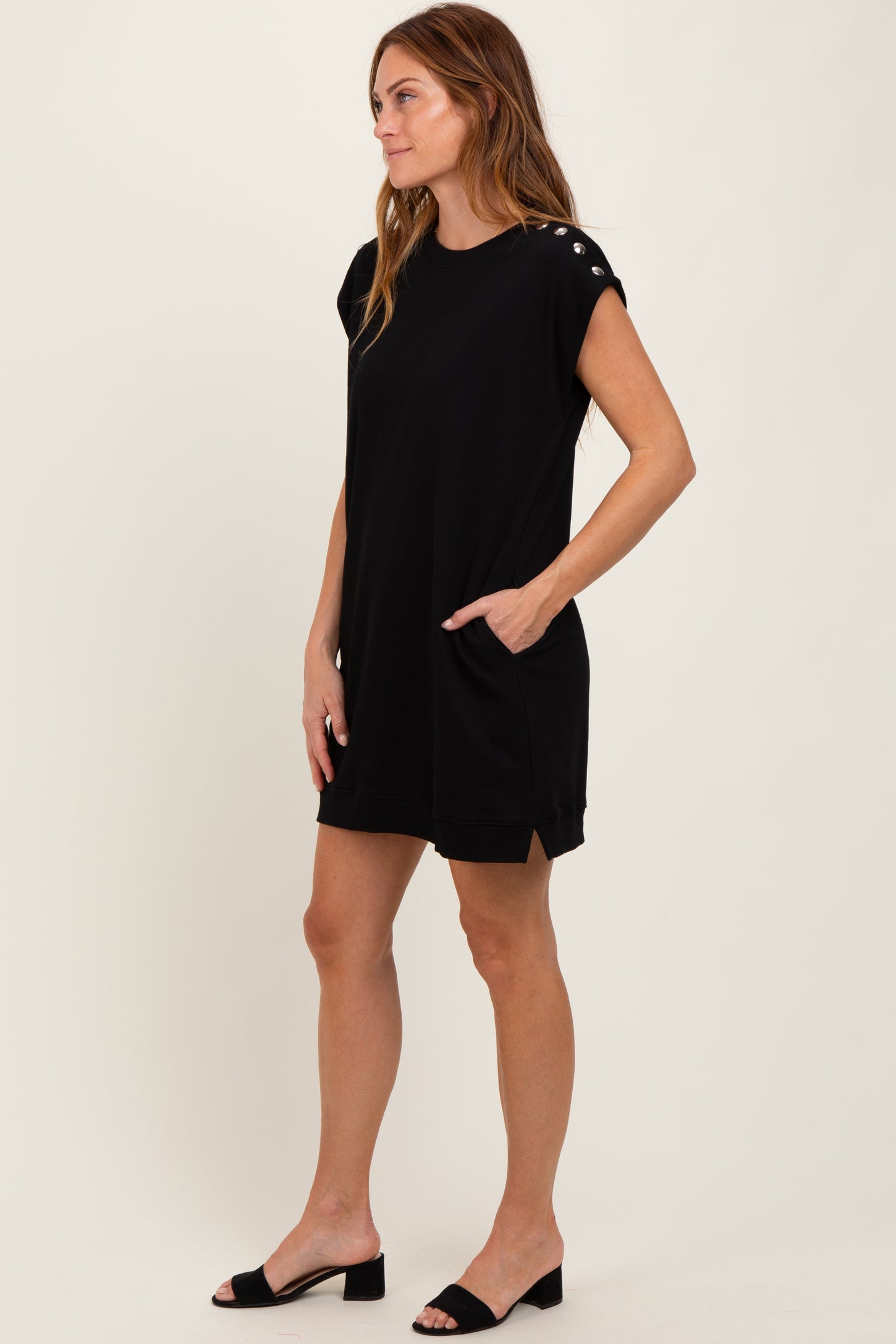 woman wearing a black short sleeve dress with side pockets and button details on the shoulders