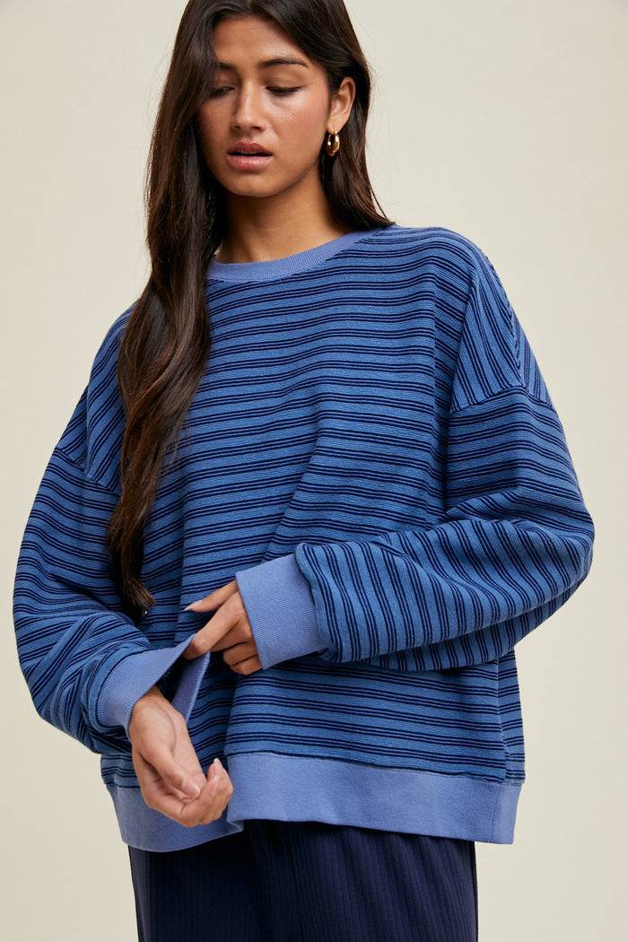 woman wearing a blue striped oversized sweatshirt with long sleeves and a relaxed fit