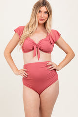 woman wearing a rose pink maternity bikini with ruffled sleeves and high-waisted bottoms, showcasing her baby bump