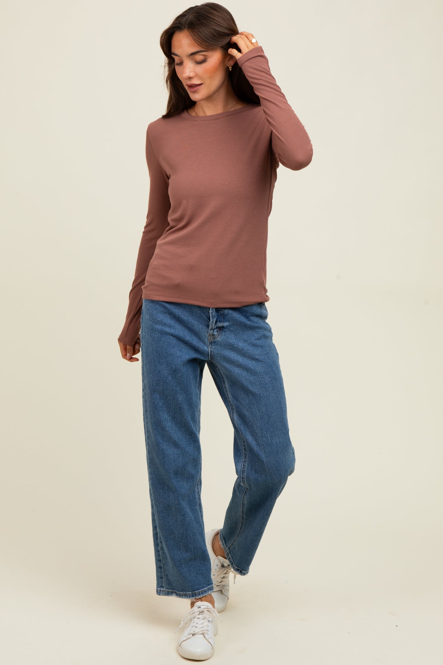 woman wearing a brown long sleeve top paired with high-waisted blue wide leg jeans and white sneakers