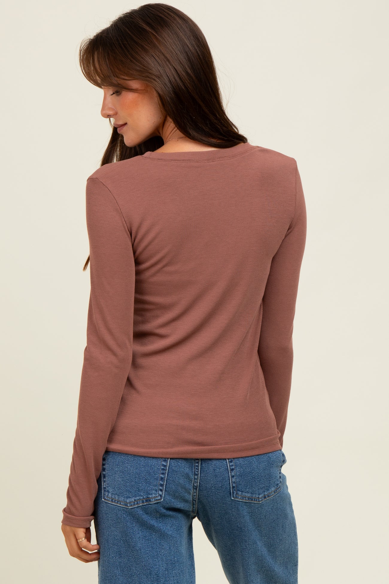 woman wearing a rust long sleeve ribbed top, facing away, tucked into high-waisted denim jeans