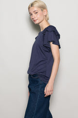 woman wearing a navy blue short sleeve top with ruffle details, paired with dark denim jeans