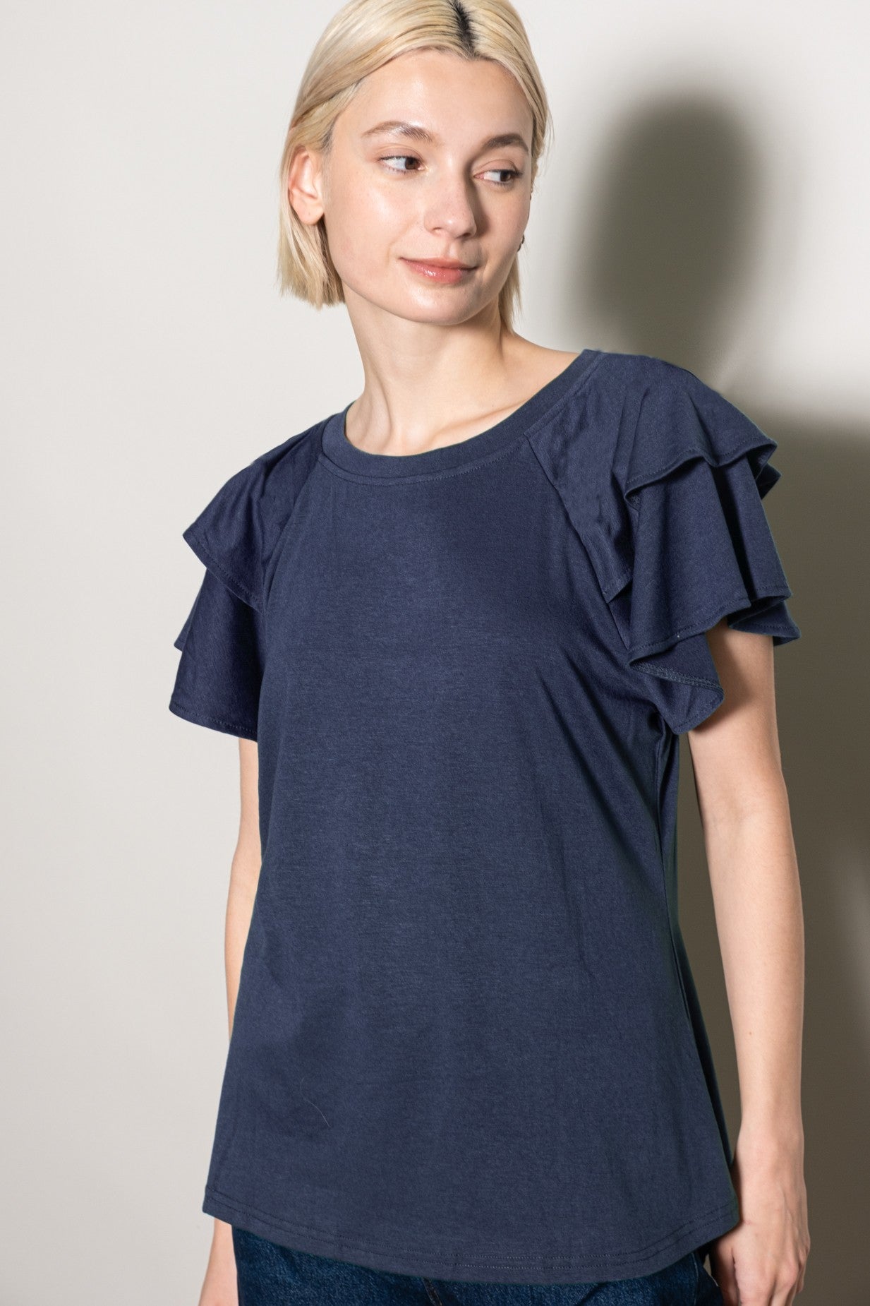 woman wearing a navy blue short sleeve top with ruffled sleeves and a relaxed fit