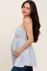 woman wearing a light blue strapless smocked maternity top, holding her baby bump