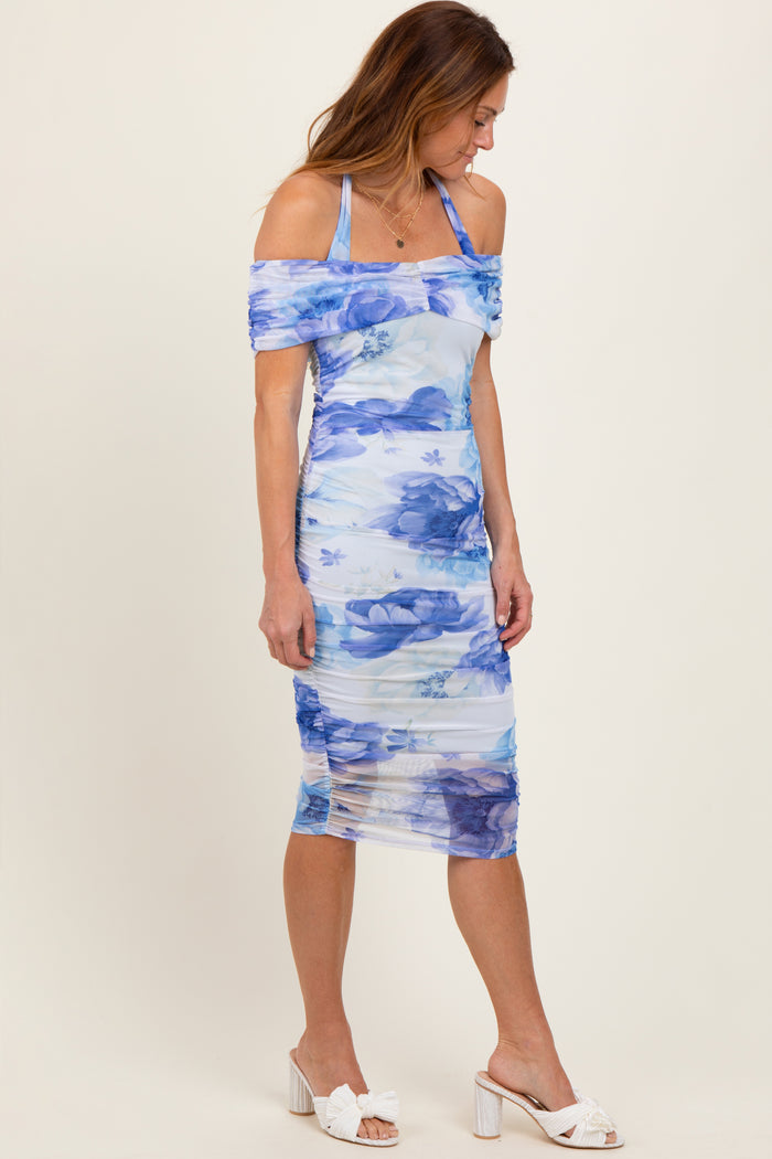 woman wearing a blue floral off-the-shoulder midi dress with ruching and strappy details, paired with white heels