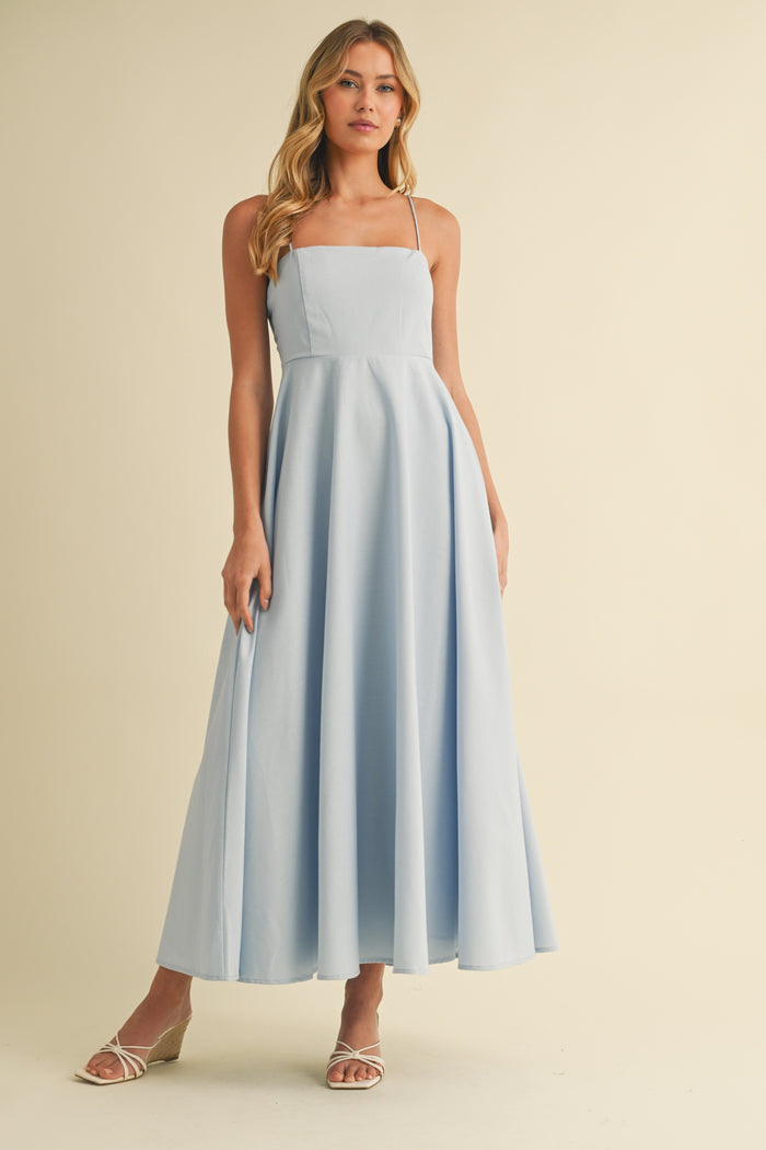 woman wearing a light blue spaghetti strap maxi dress with a fitted bodice and flowy skirt