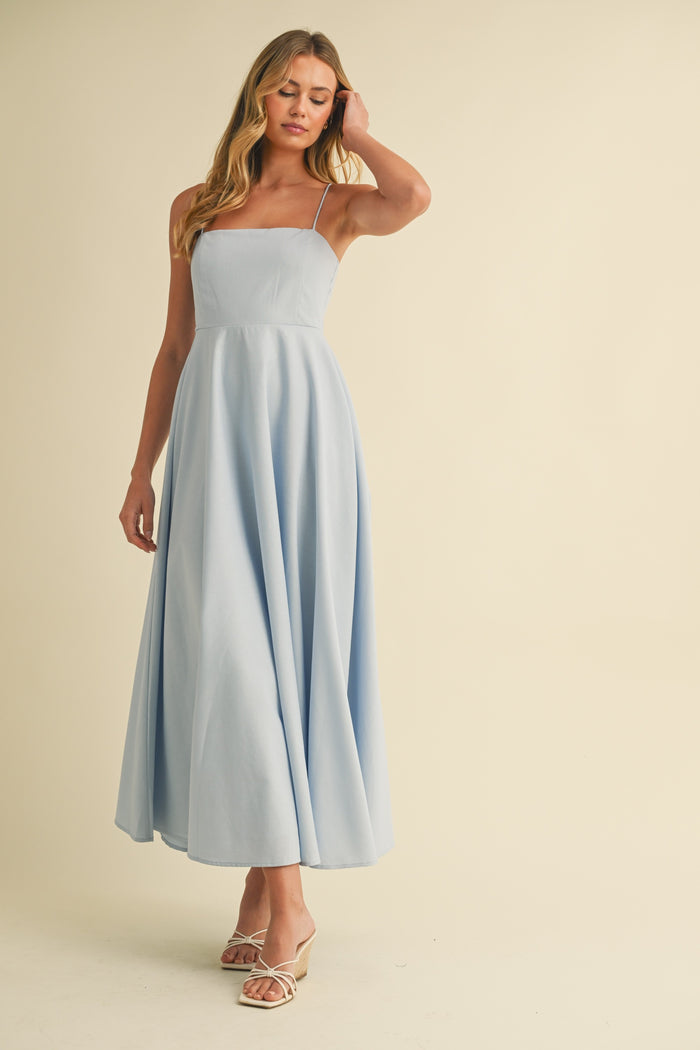 woman wearing a light blue spaghetti strap maxi dress with a fitted bodice and flowing skirt