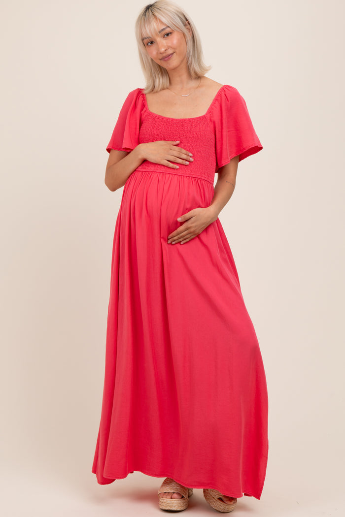 woman wearing a pink maternity maxi dress with flutter sleeves and holding her baby bump