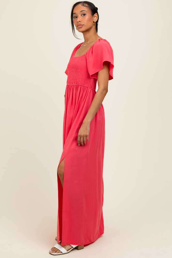 woman wearing a coral maxi dress with a smocked bodice and flutter sleeves, featuring a side slit