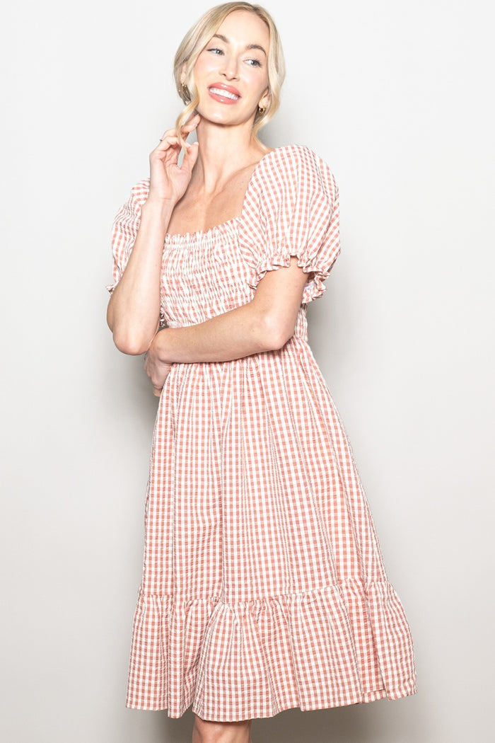 woman wearing a pink and white gingham puff sleeve dress with a square neckline and tiered hem