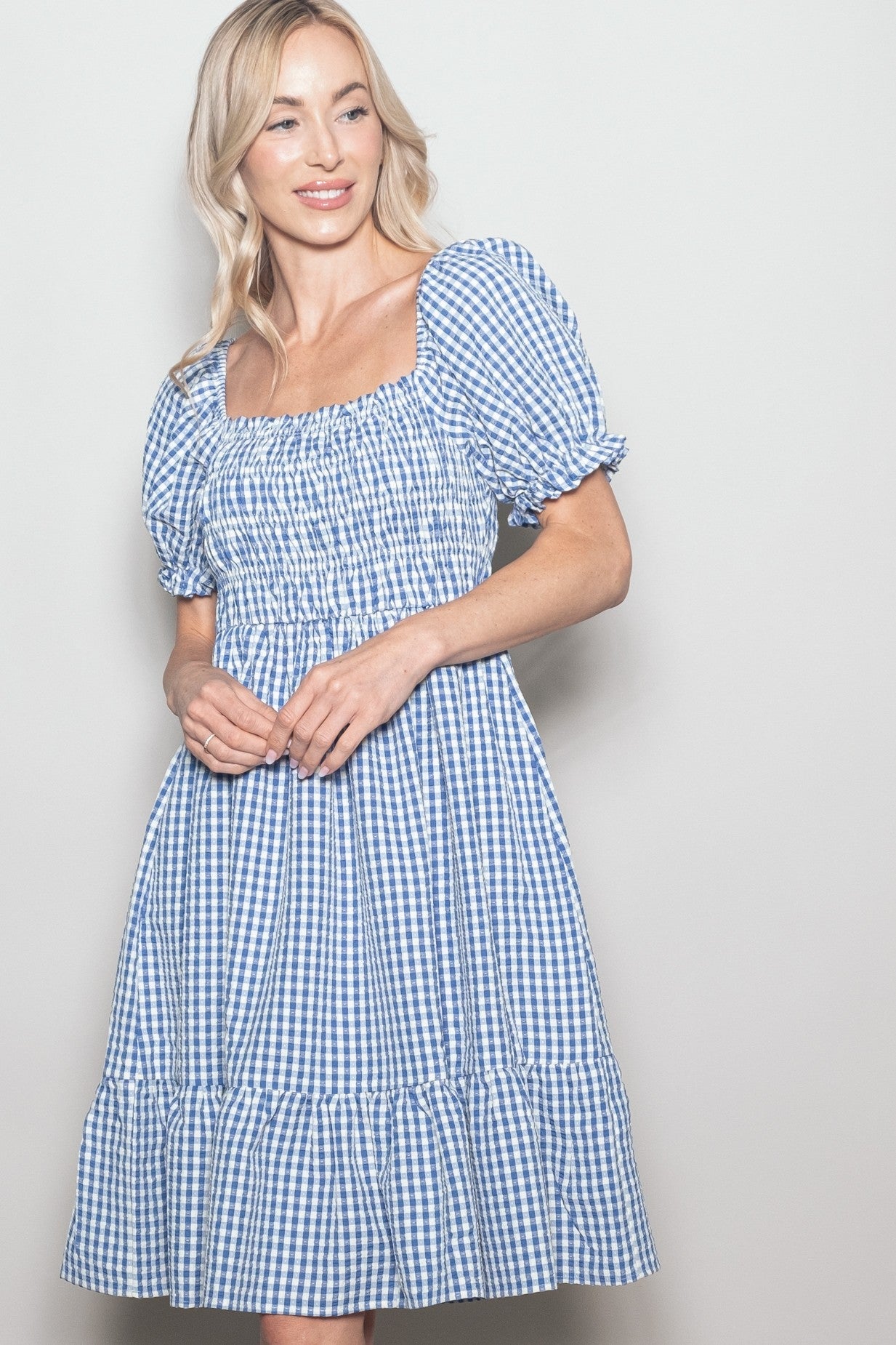 woman wearing a blue and white gingham puff sleeve mini dress with a smocked bodice and tiered skirt
