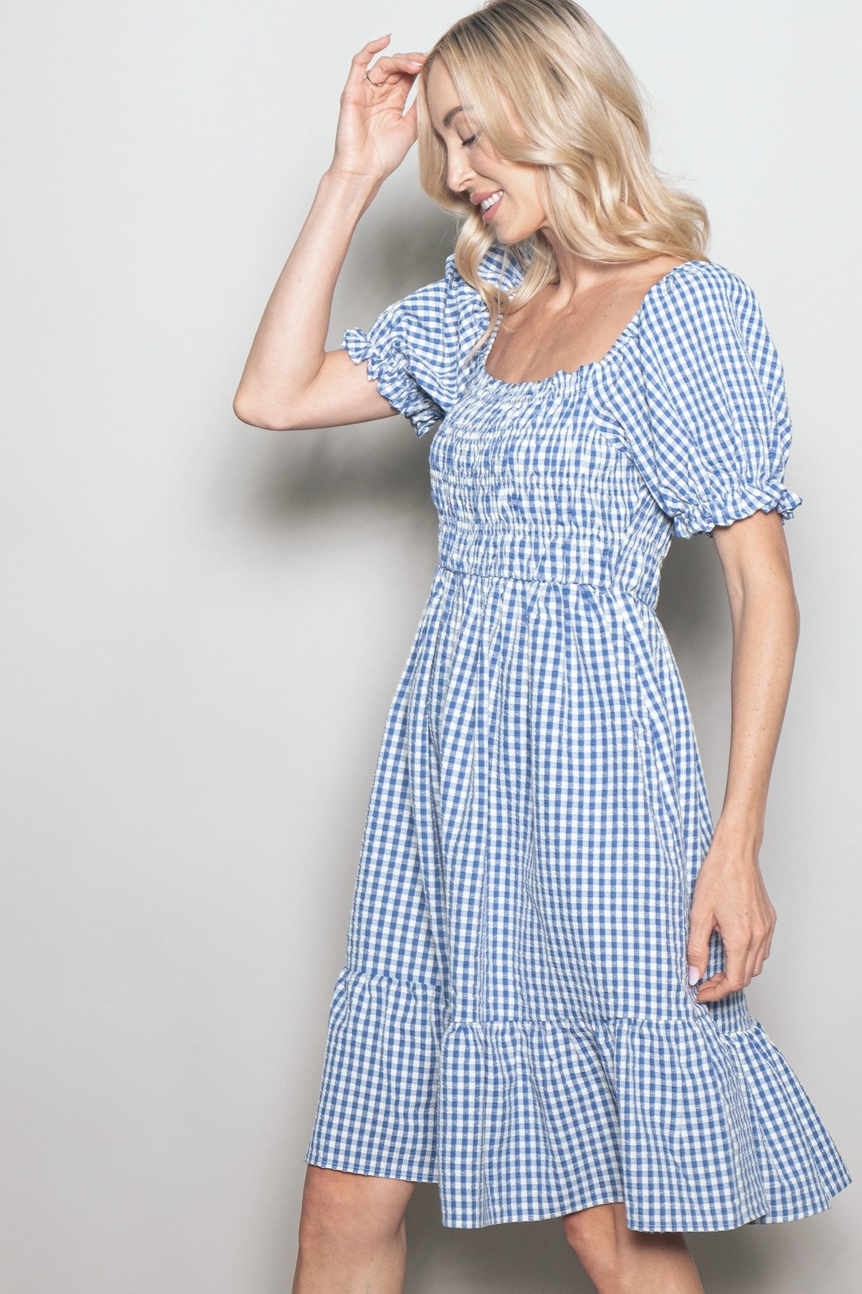 woman wearing a blue and white gingham puff sleeve dress with a ruffled hem and a square neckline