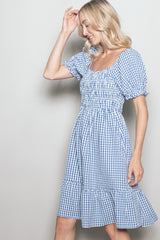 woman wearing a blue and white gingham puff sleeve dress with a ruffled hem and a square neckline