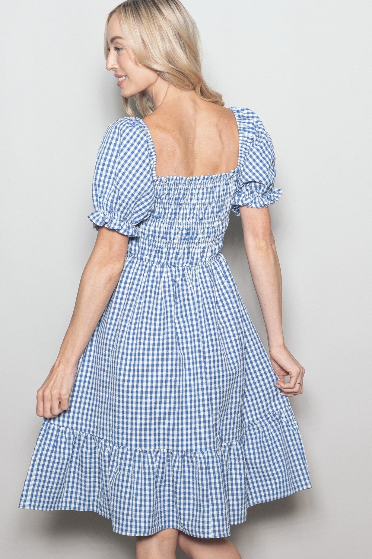 woman wearing a blue and white gingham smocked sundress with puff sleeves and a ruffled hem